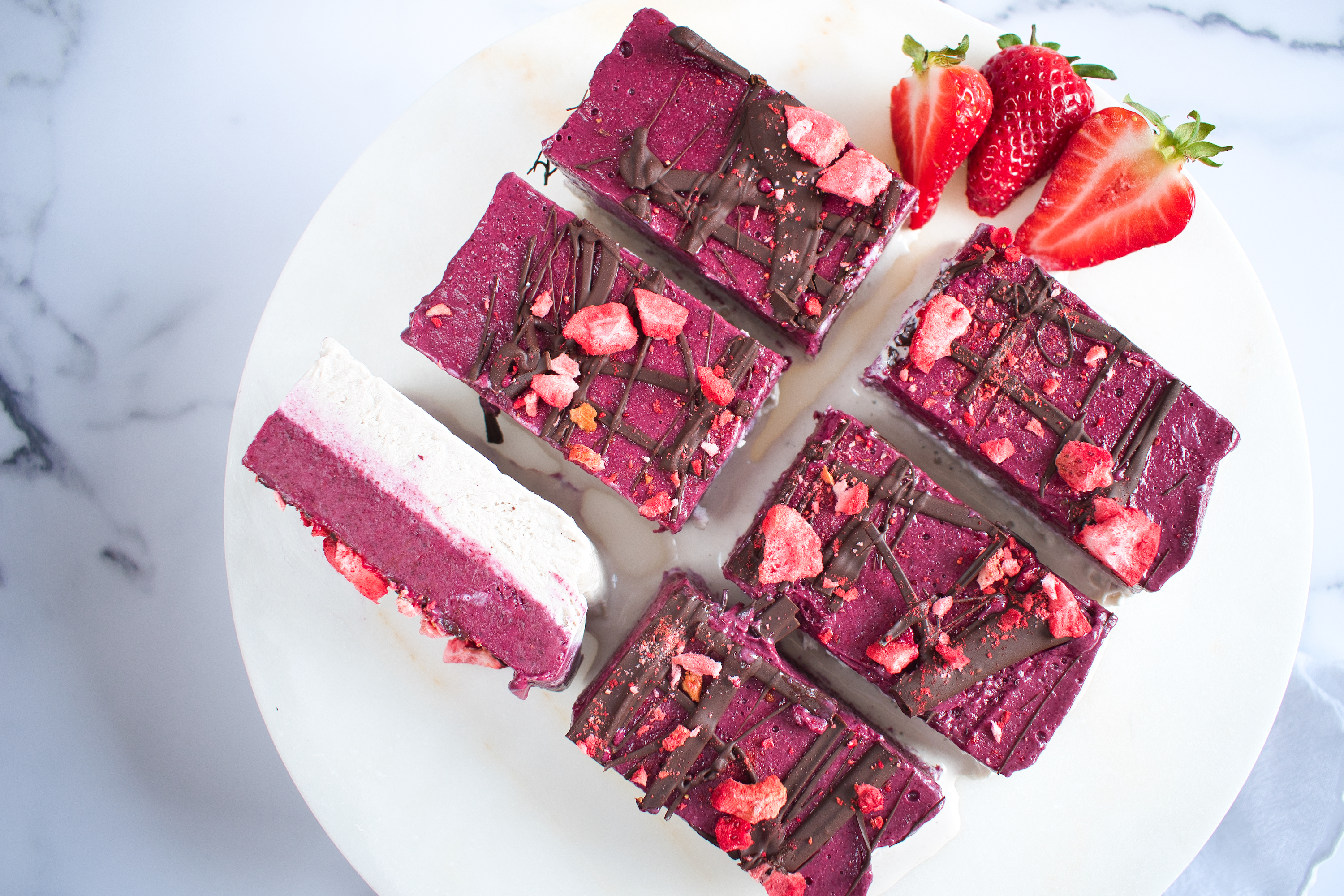 Low FODMAP berry ice-cream slice with freeze dried strawberry and chocolate drizzle on a white plate
