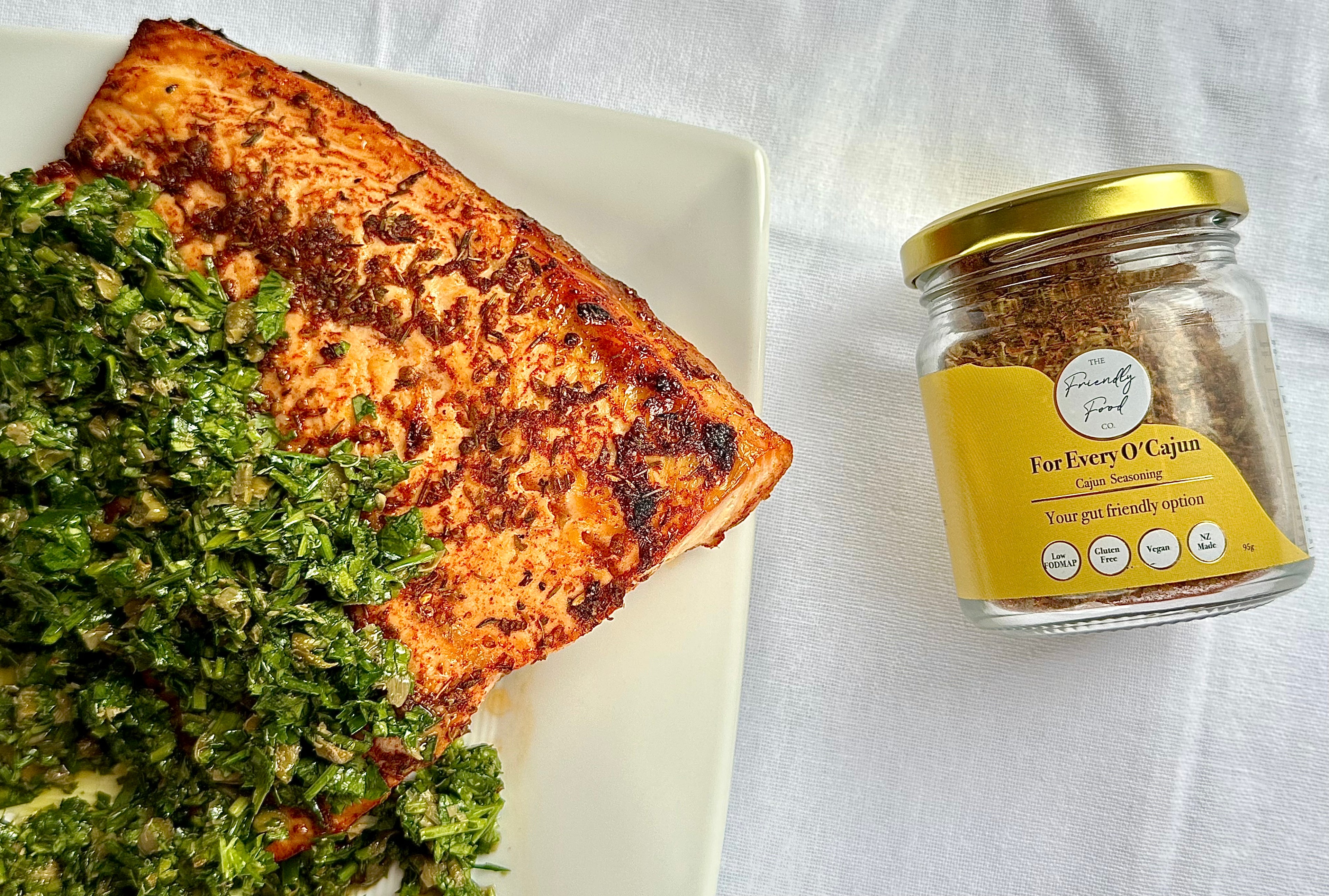Plated Low FODMAP Baked Maple Cajun Salmon with Herby Dressing with a jar of The Friendly Food Co. For Every O'Cajun seasoning on a white background