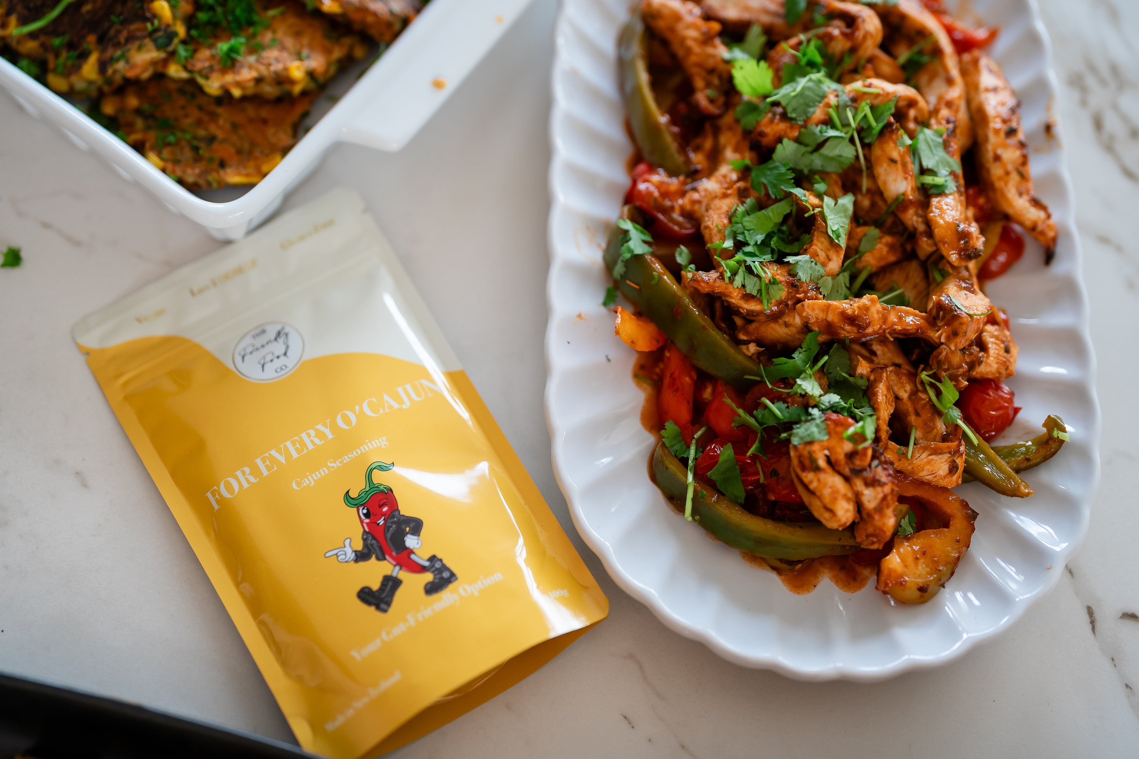 Plated dish of chicken and vegetables with For Every O'Cajun Seasoning  on a white surface.