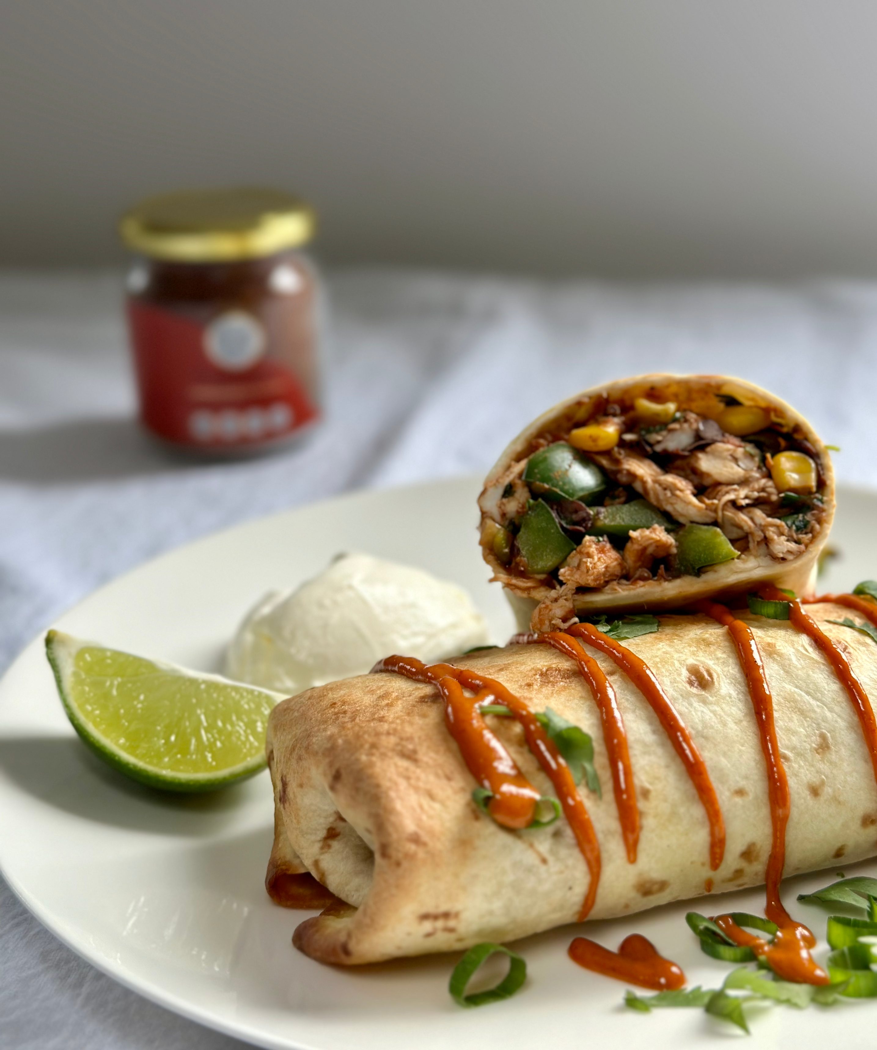 Low FODMAP Chicken Chimichangas with a side of sour cream and lime, with a jar of The Friendly Food Co Na'Cho Problem spice mix. 
