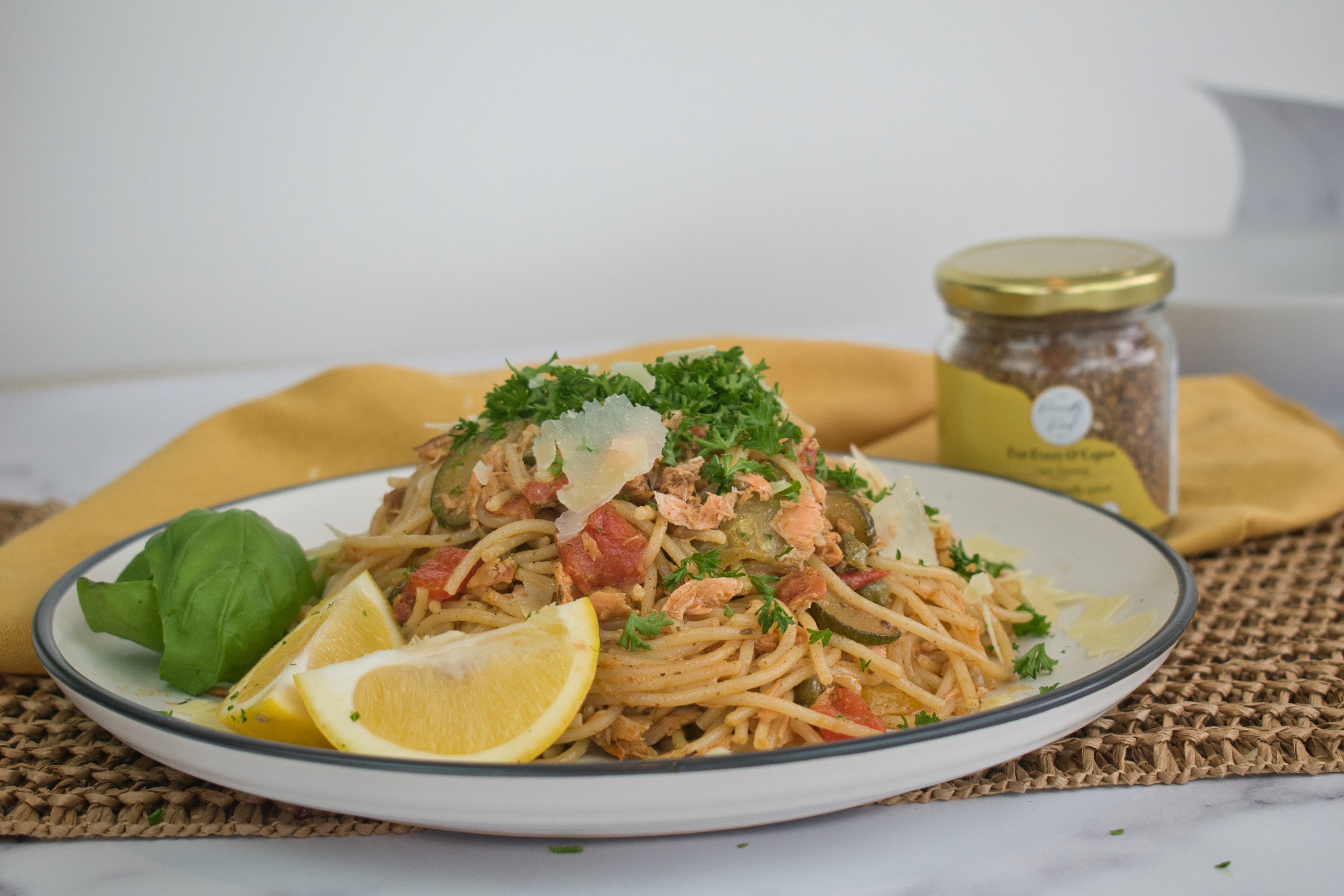Low FODMAP Creamy Salmon Pasta on a white plate, with a jar of The Friendly Food Co, For Every O'Cajun seasoning in the background.