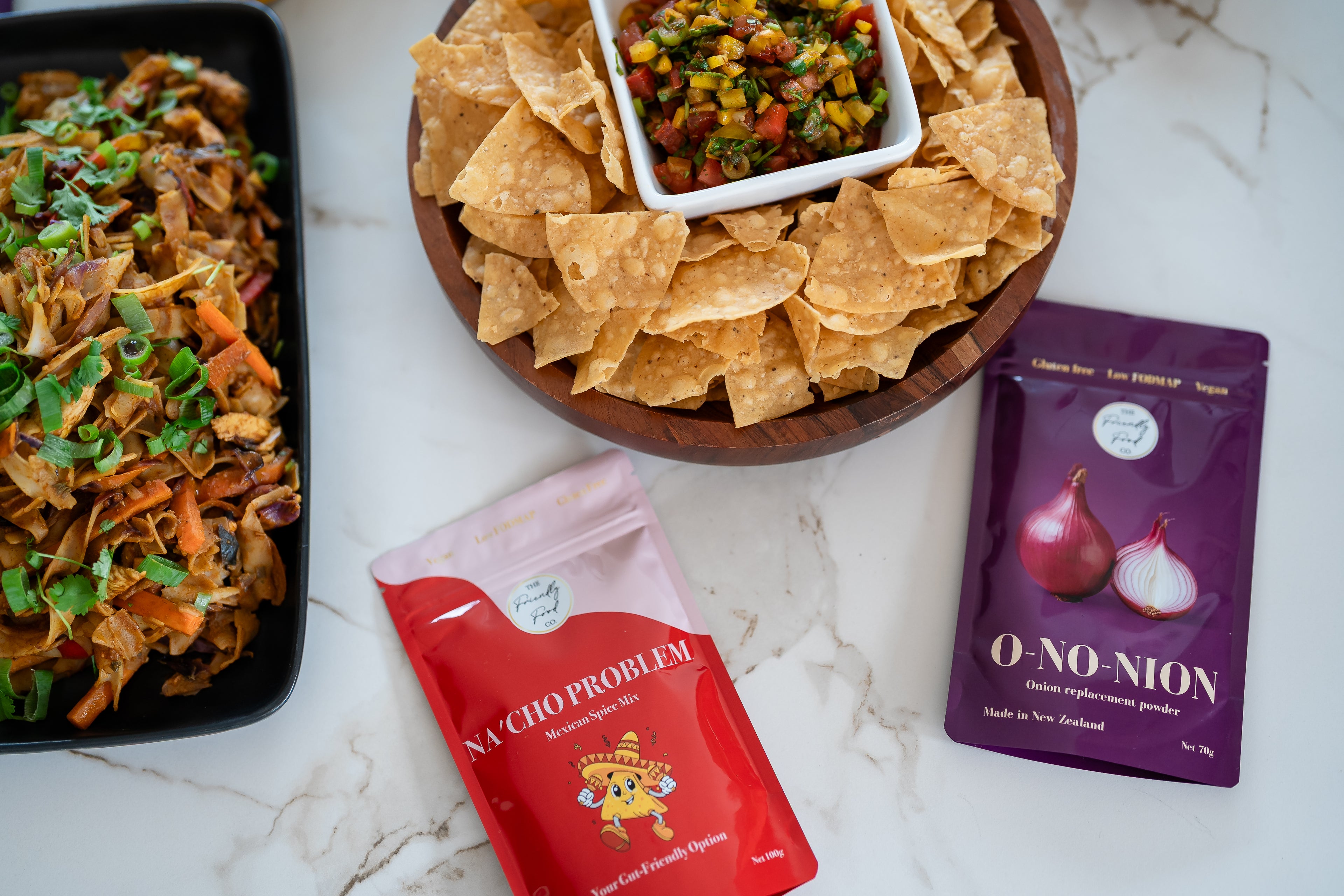 Snack platter with chips and salsa, and two packets of low fodmap seasoning on a marble surface