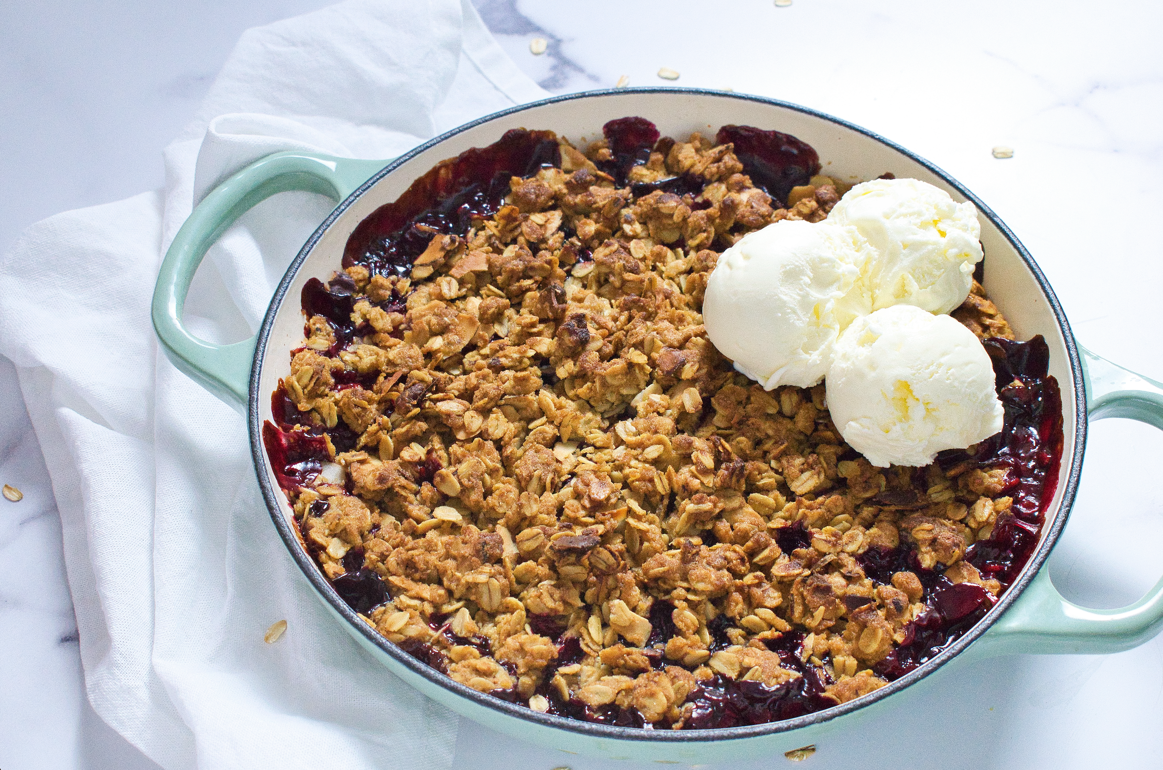 Blue dish with Low FODMAP Mixed Berry and Rhubarb Crumble and vanilla ice cream on a white background