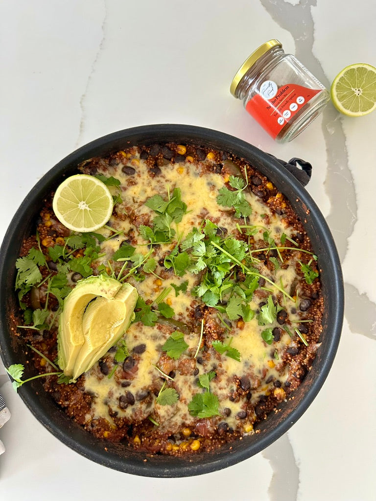Skillet with Low FODMAP One Pan Mexican Quinoa topped with avocado, lime, and a jar of The Friendly Food Co. Mexican seasoning on a light background