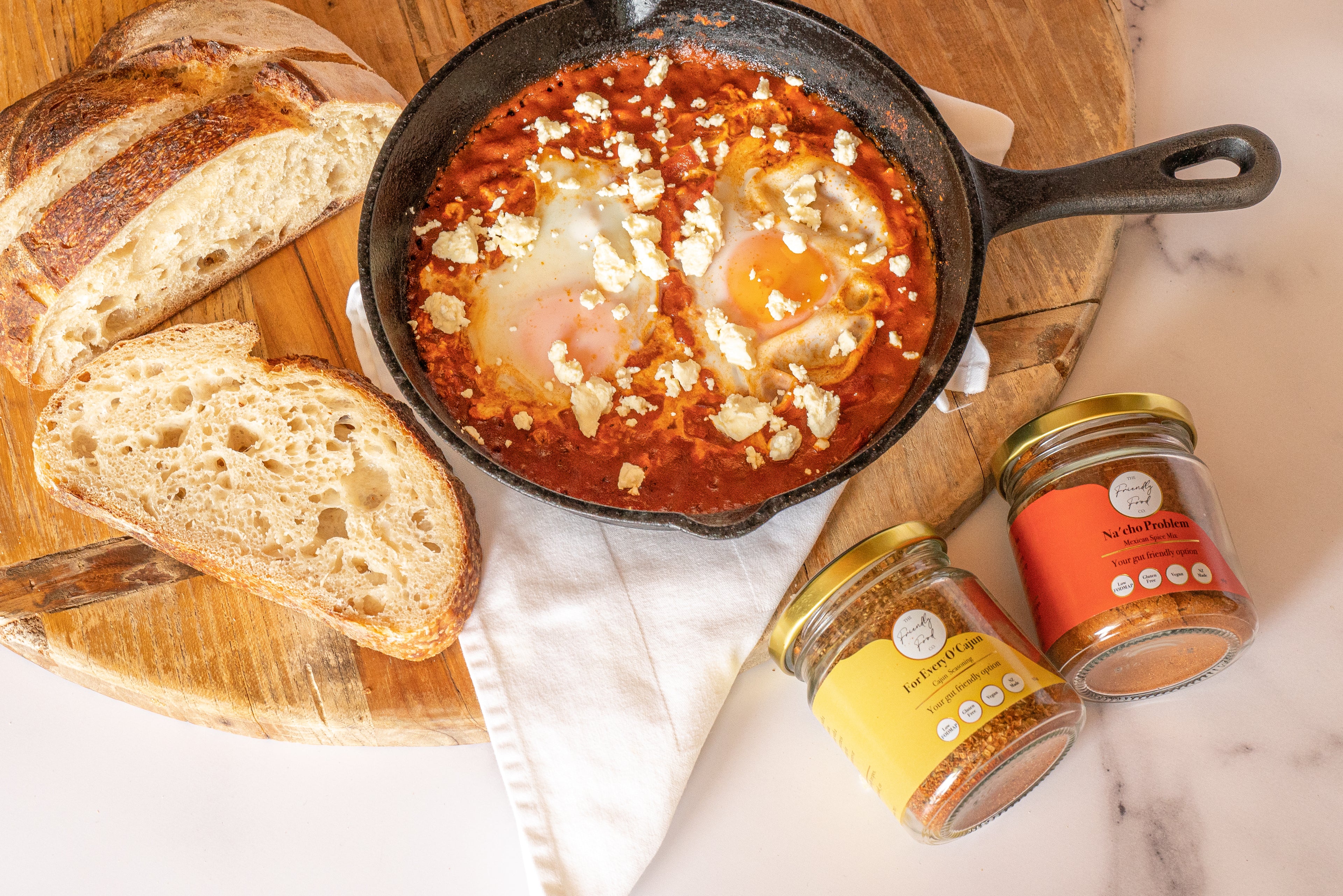 Low FODMAP Shakshuka with sourdough and The Friendly Food Cp. seasoning jars on a wooden board