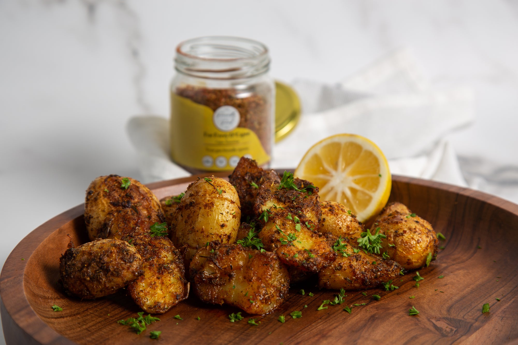 Wooden plate with Low FODMAP Smashed Crispy Cajun Potatoes and a jar of Cajun seasoning on a white background