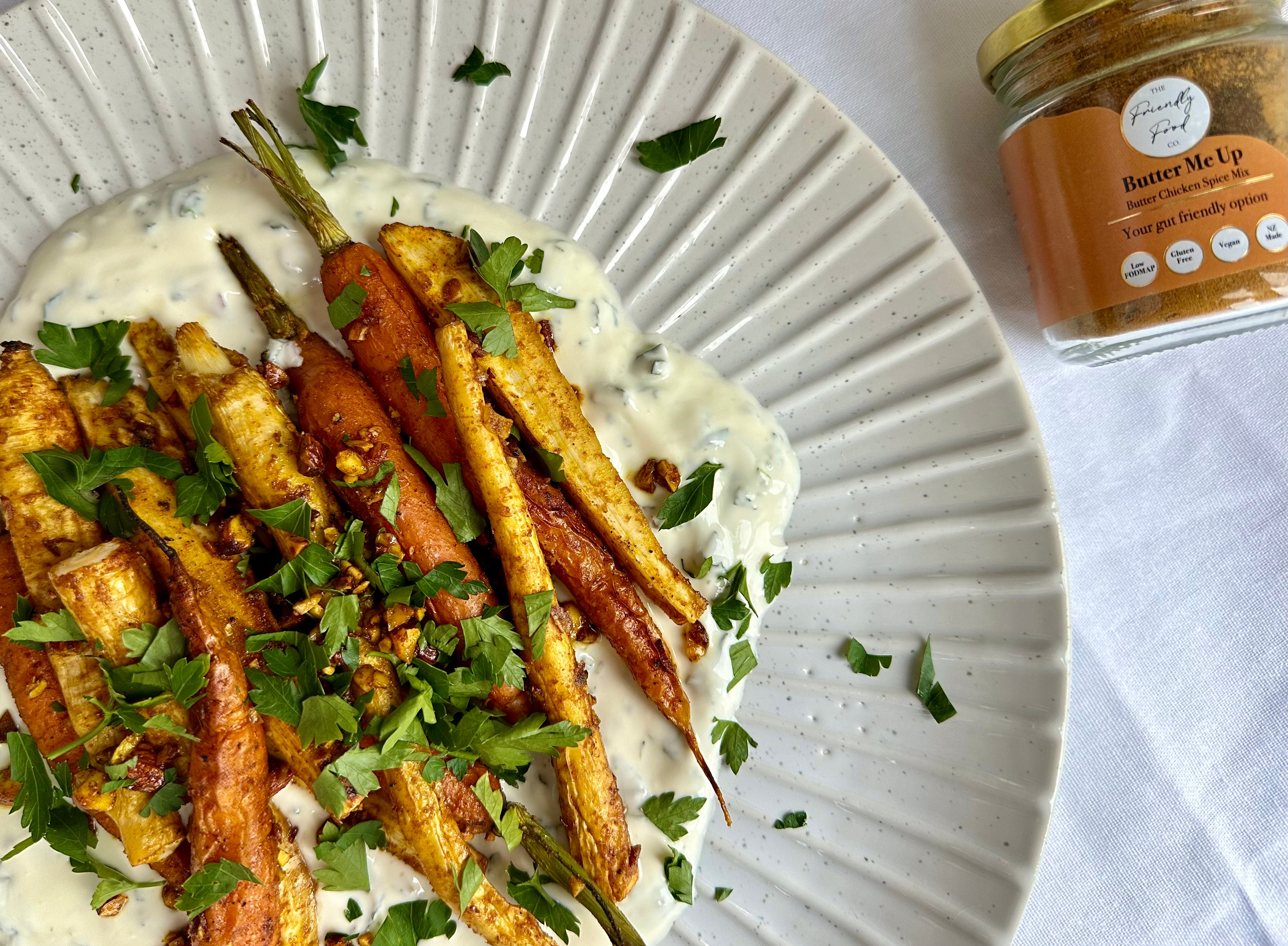 Plate of rpiced Roast Carrots and Parsnips with a mint yoghurt dressing, next to a jar of The Frienldy Food Co. 'Butter Me Up' spice mix
