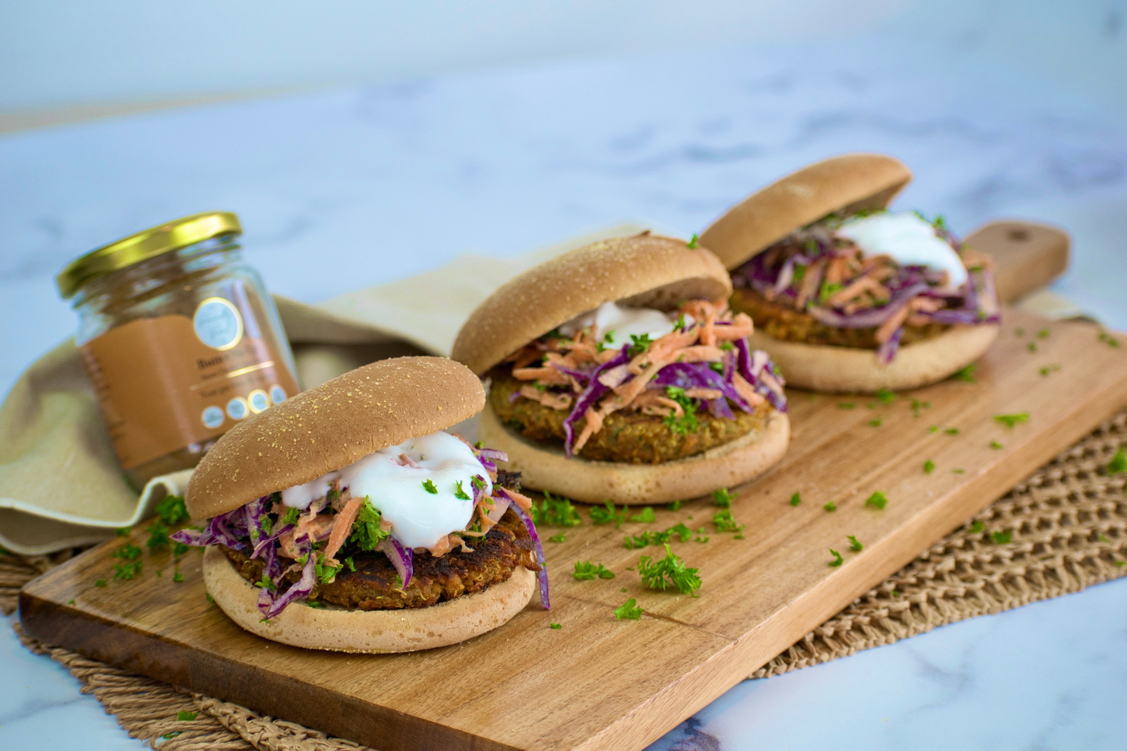 Low FODMAP, Vegan Lentil and Quinoa Curried Burgers with Tahini Slaw on a wooden board with a jar of The Friendly Food Co. Butter Me Up spice mix in the background.