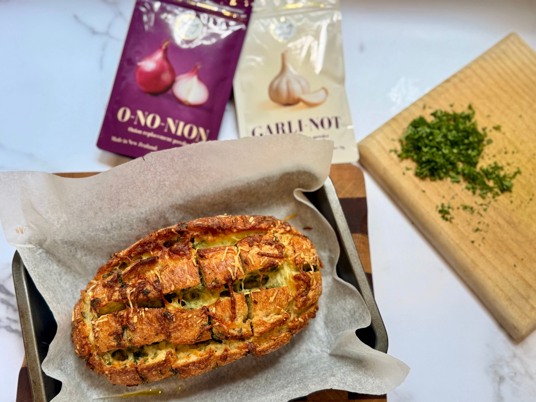 Low FODMAP cheesy pull apart garlic bread on a tray with 'O-No-Nion' and 'Garli-Not' packaging in the background