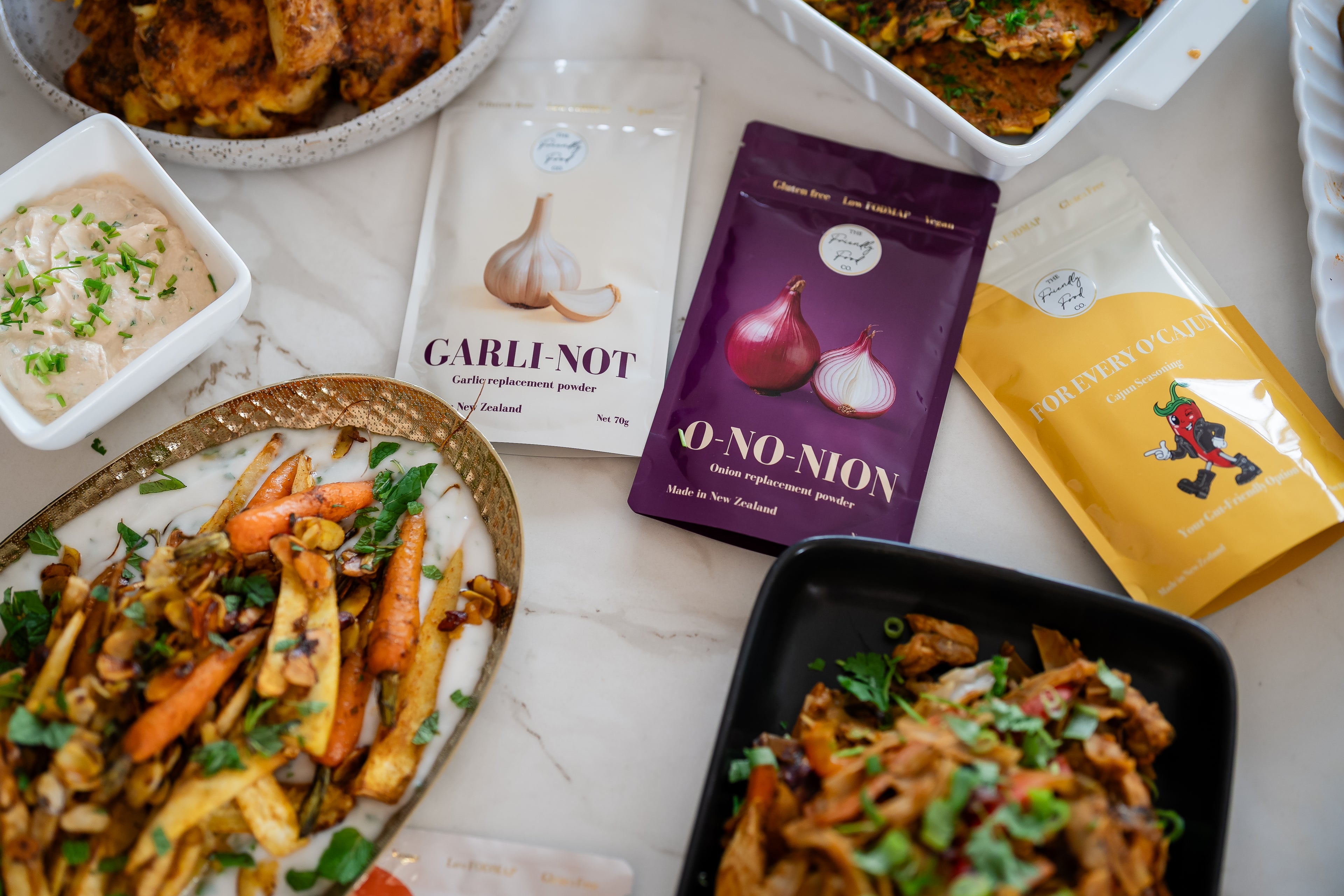 Assorted food packages including garlic and onion replacement powders on a marble surface with plated dishes.