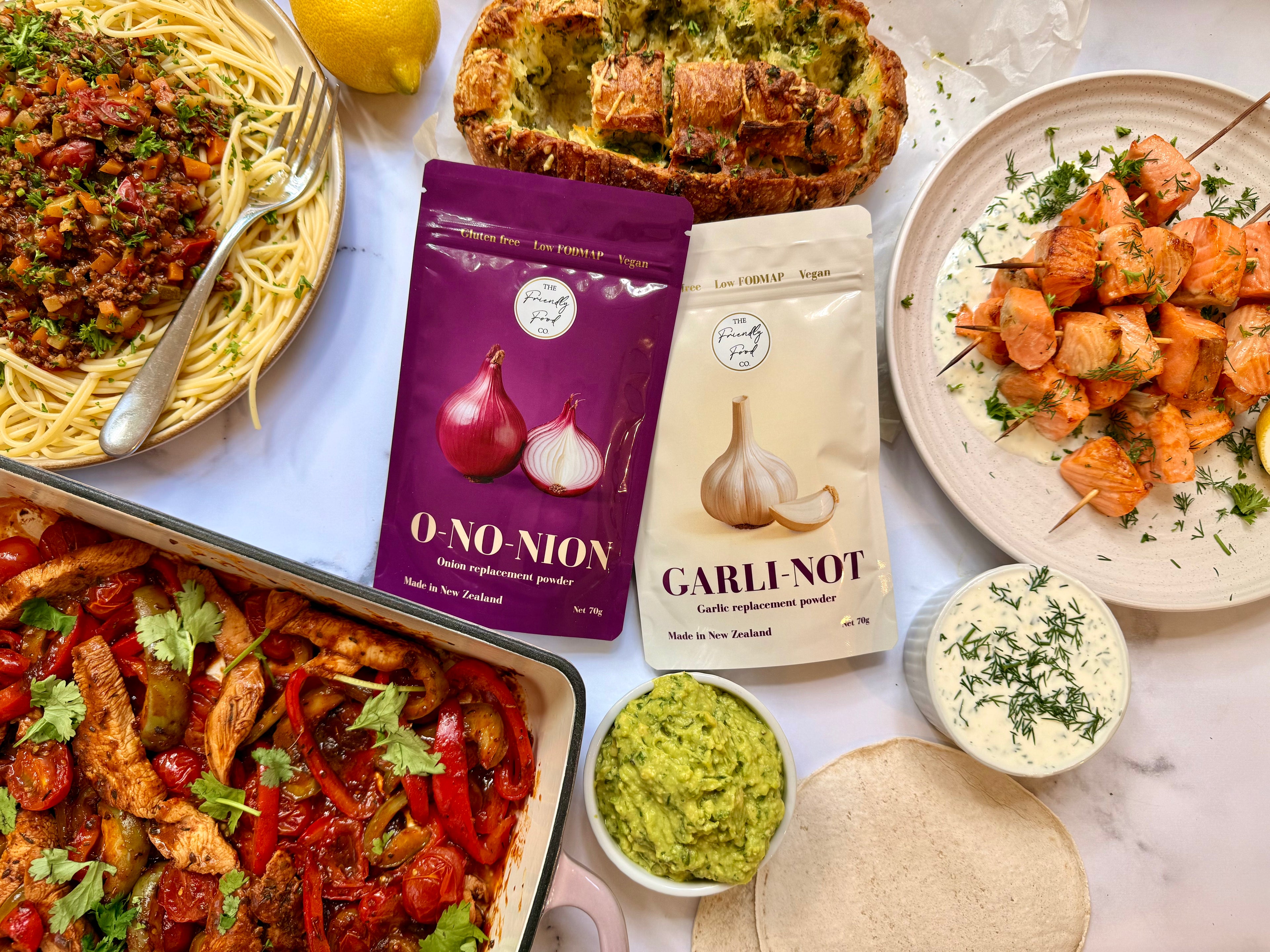 Assorted food items including pasta, skewers, and packaged Low FODMAP garlic and onion replacement powders on a marble surface.
