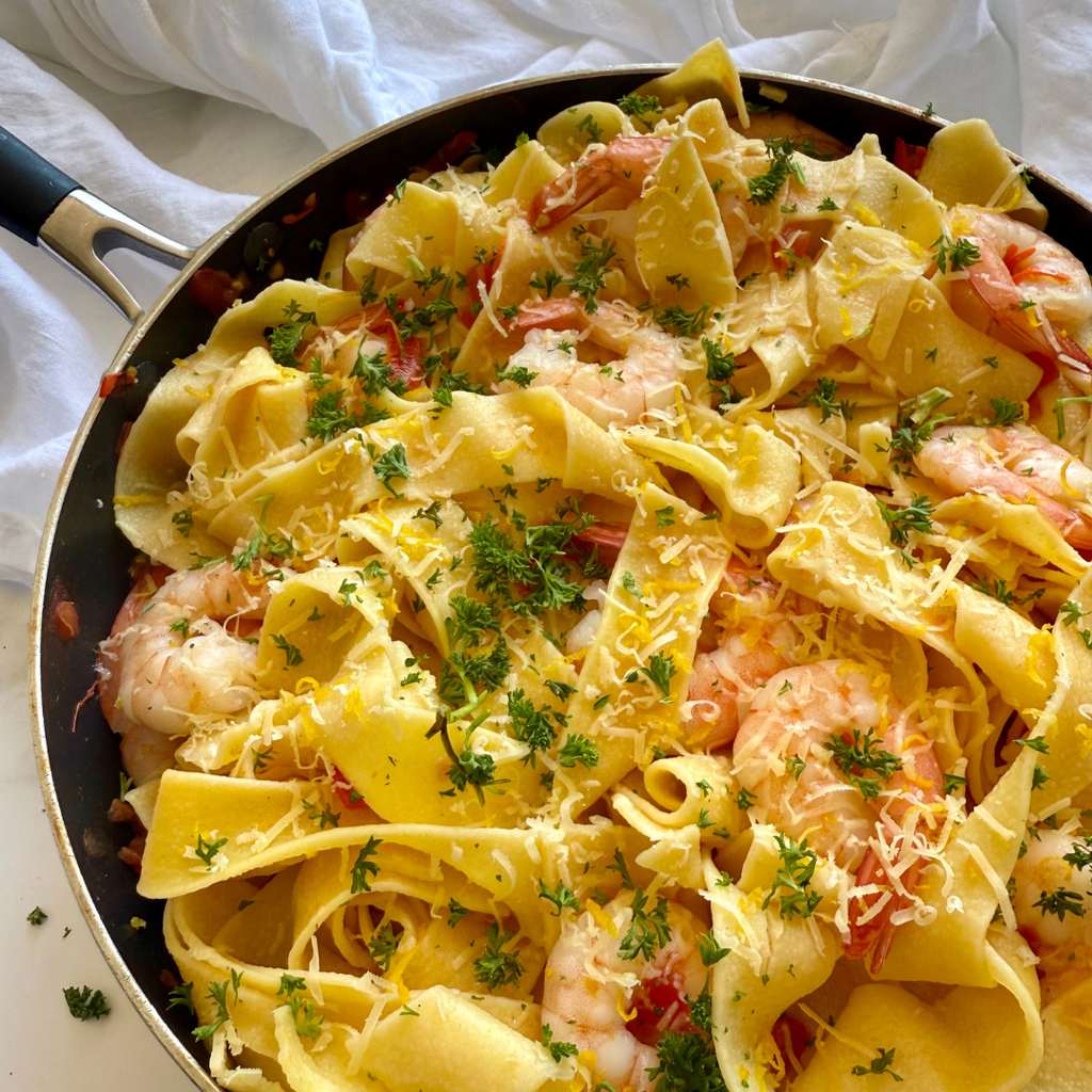 Low FODMAP fettuccine prawn pasta with lemon, parmesan and parsley in a pan on a white background