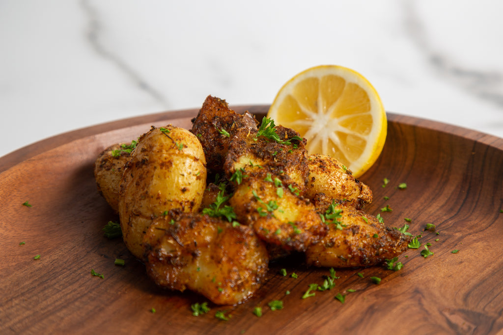 Low fodmap smashed cajun potatoes with lemon wedge on a wooden plate