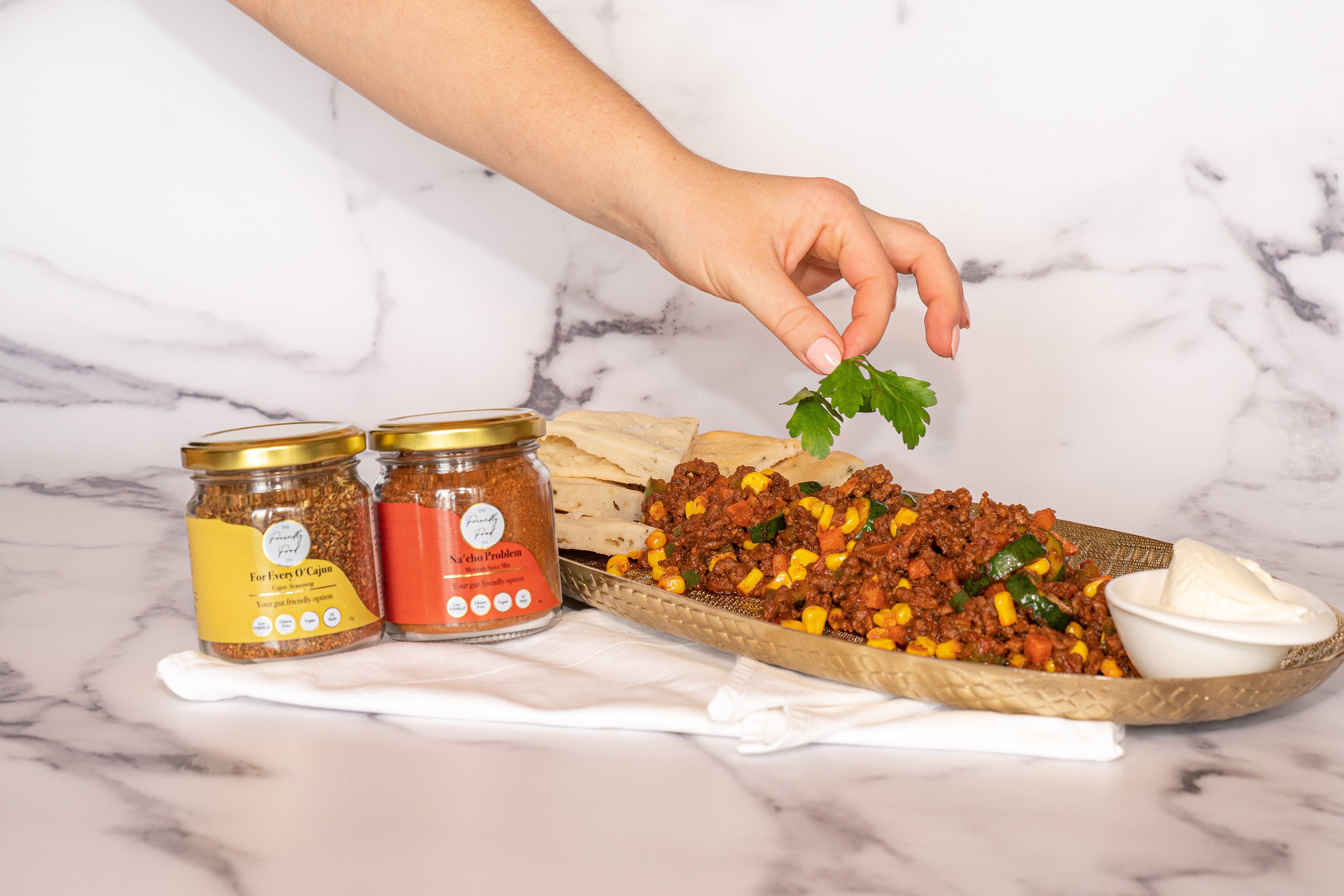Garnishing Low FODMAP Mexican Spiced Lamb Mince with The Friendly Food Co Mexican and Cajun seasoning on a marble surface