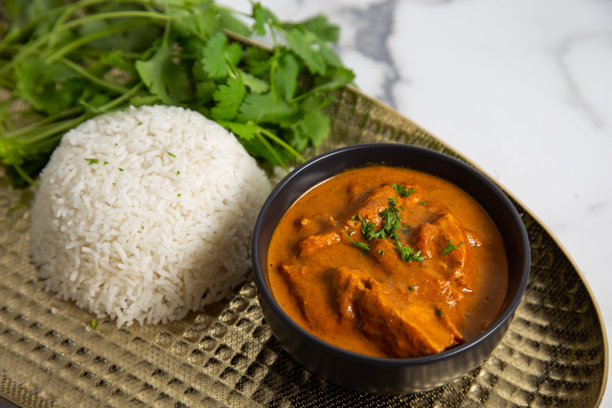 Bowl of Low FODMAP Butter Chicken Curry with rice and herbs on a textured surface