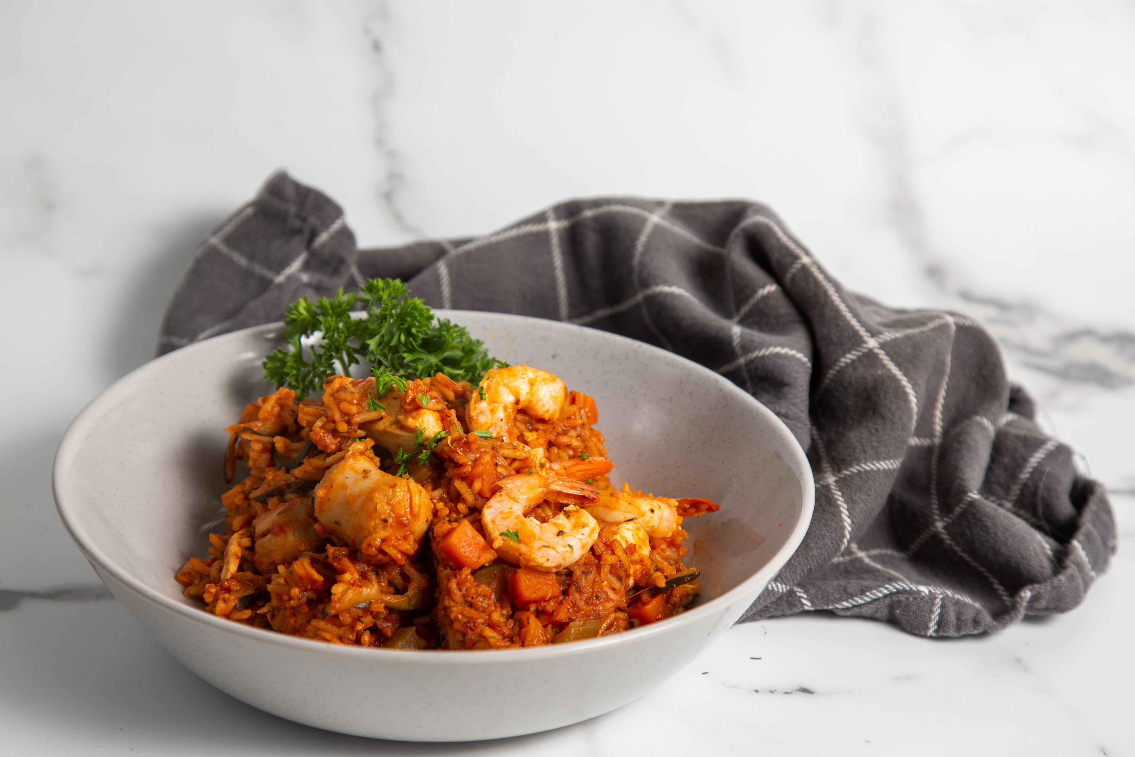 Bowl of low FODMAP Jambalaya with a gray napkin on a marble surface